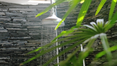 Summer shower head water spray in beautiful bathroom with tropical plants on sunny dayの写真素材