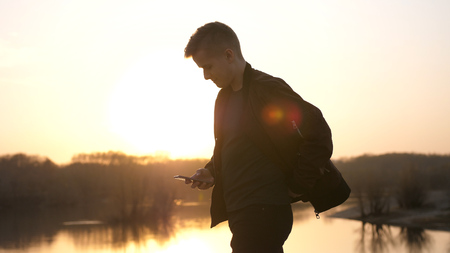 Young man uses smart phone at beautiful sunset on the beach.の写真素材
