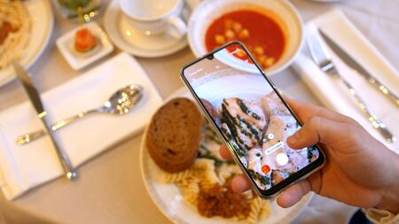 Hands using smartphone taking photos of chicken pasta with tomato coup and piece of breadの写真素材