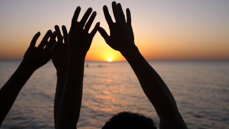 Happy family raising hands up. Hands up in the air silhouette over sunset sky. Vacation concept.の写真素材