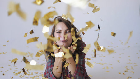 Beautiful woman blowing gold glitter confetti on a white backgroundの写真素材