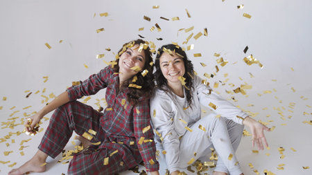 Beautiful happy women sitting under gold glitter confetti on a white background