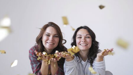 Two beautiful girls blowing gold glitter confetti on a white backgroundの写真素材