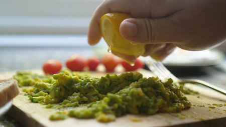 Close up Of Hand Squeezes Lemon Juice Over Avocado Toast. Breakfast Time, Healthy Food.