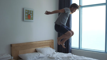 Handsome man have fun, jumping, dancing on bed by the windowの写真素材