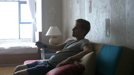 Handsome Young Man at Home Sitting on a Couch Watches TVの写真素材