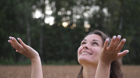 Close up portrait of pretty woman looking up at rain in nature. Young woman rejoices in the summer...
