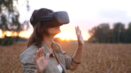 Beautiful girl in a golden wheat field uses virtual reality glasses in the sunsetの写真素材