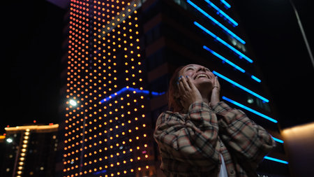 Young woman is very emotionally looking at glowing houses on the street of the evening city admires...