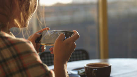Close up of woman holds modern smartphone and taking pictures of her morning breakfast coffee and tasty croissant buns to share photos on social media resourcesの写真素材
