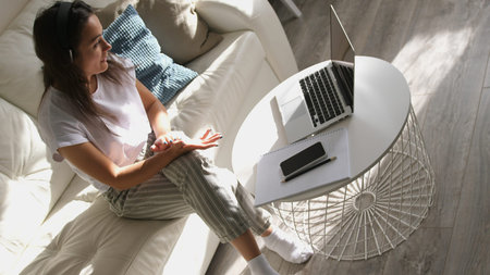 Young woman wears headset conference calling on laptop talks with online teacher studying, working...