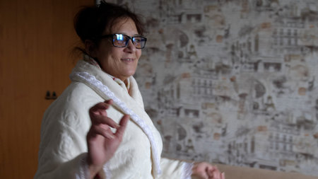 Elderly cheerful woman in glasses listening to music on a phone and dancing at home