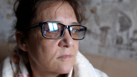 Thoughtful woman in 60s in glasses looking out window absorbed in problems and difficulties....