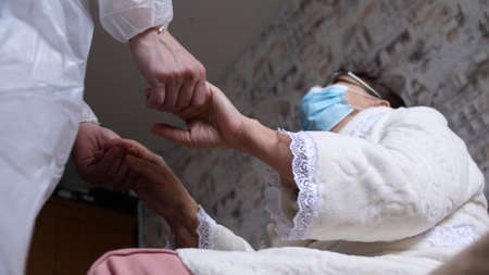 Doctor in a protective suit Helping Elderly sick woman wearing medical mask At Home. Assistance And Elderly Care Concept.の写真素材