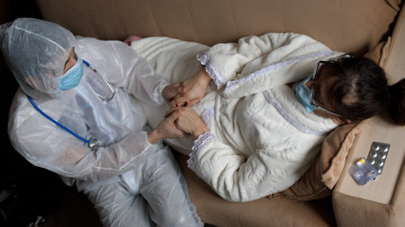 Care of the doctor in protective suit and medical mask for the patient. Hands of an old woman in the arms of a doctor. Service and support for the elderly. Assistance, Seniors Concept.の写真素材