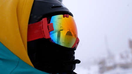 Man in a helmet and glasses riding a mountain on a lift with a snowboard on a background of snowfall.の写真素材