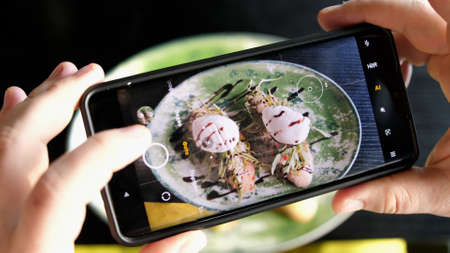 A woman in a restaurant takes a picture of food with a mobile phone camera. Sandwich with poached egg and avocado and salmonの写真素材