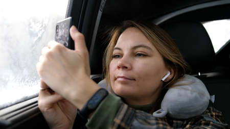 Travel concept. Young woman sitting with pillow on mobile phones in cars. 4k Resolution.の写真素材