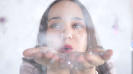 Portrait smiling young brunette woman blowing confetti from hands. Romantic feeling. Joyful flirting teenager girl.の写真素材