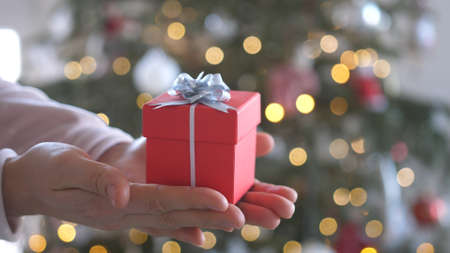 Woman hands holding red gift box presents with silver ribbon bow. Concept Season of giving, Christmas, happy new year, Birthday, Valentine, Anniversary, Mothers day.の写真素材