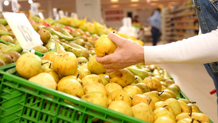 Elderly woman chooses ripe organic pears in the supermarket. Woman picks ripe organic pears in the supermarket during quarantine.の写真素材
