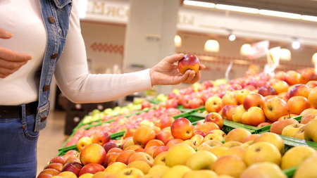 Elderly woman chooses apple fruits vegetables on the counter in supermarket.の写真素材