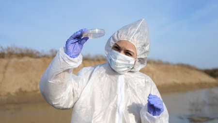 Scientist or ecology expert in protective costume with test tube taking probe for quality control from dirty contaminated water in toxic dangerous zone.の写真素材