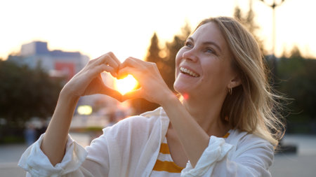 happy woman making a heart shape from her hands in the city on a sunny day during sunsetの写真素材