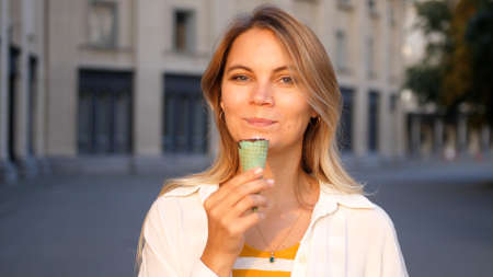 Beautiful woman eating ice cream in the city park in summer bright day. Outdoor walking, relax and leisure in nature in public parkの写真素材
