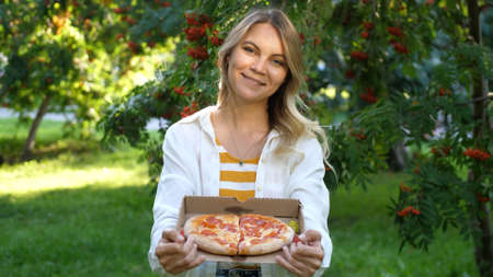 Young beautiful brunette woman holding box with italian pizza in summer parkの写真素材
