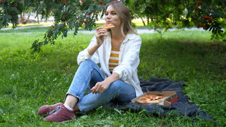 Young woman outdoors eating italian pizza sits on the plaid in a parkの写真素材