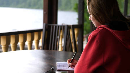 Woman writing her thoughts on the sheet of paper on wood table beside a river.の写真素材