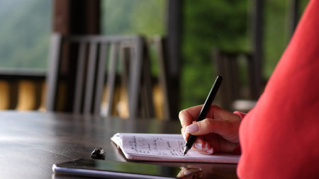 Woman hand is writing her thoughts on the sheet of paper on wood table beside a river.