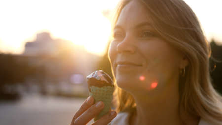 Beautiful woman eating ice cream in the city park in summer bright day. Outdoor walking, relax and leisure in nature in public parkの写真素材