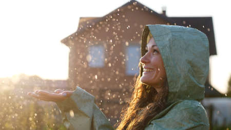 Young happy woman wearing green raincoat is feeling free and smiling under the rain. Concept of life, freedom, nature, adventure, purity.の写真素材