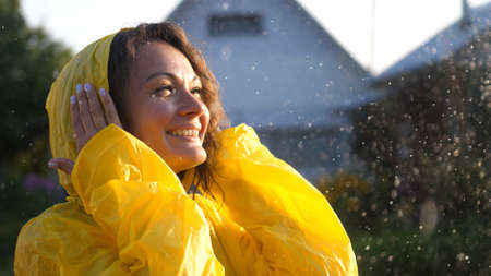 Young happy woman wearing yellow raincoat is feeling free and smiling under the rain. Concept of life, freedom, nature, adventure, purity.の写真素材