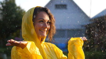 Young happy woman wearing yellow raincoat is feeling free and smiling under the rain. Concept of life, freedom, nature, adventure, purity.の写真素材