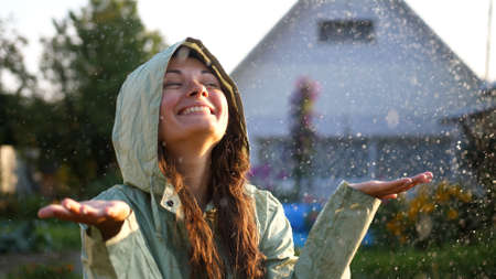 Young happy woman wearing green raincoat is feeling free and smiling under the rain. Concept of life, freedom, nature, adventure, purity.の写真素材