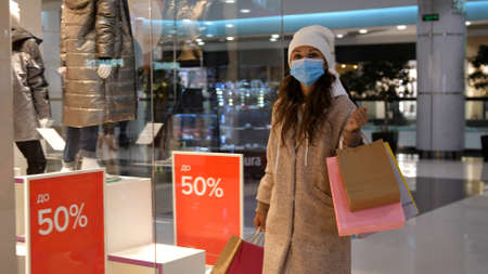 Pretty girl in mask walking in centre mall with shopping bagsの写真素材