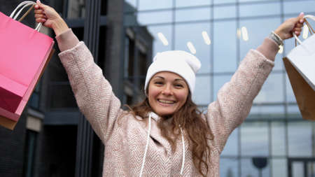 Happy girl raises hands and holds the multi-colored shopping bags in the streetの写真素材