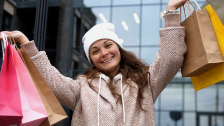 Happy girl holds and looks out of the multi-colored shopping bags in the streetの写真素材
