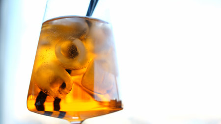 Hand mixes an orange drink with black cocktail tube. Glass of orange soda with iceの写真素材