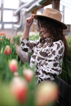Young beautiful woman in hat posing looks at flowers in a greenhouse Tulipsの写真素材