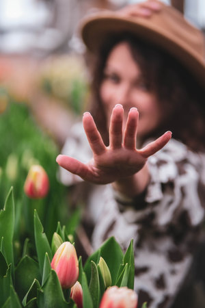 Young beautiful woman in hat posing looks at flowers in a greenhouse Tulips