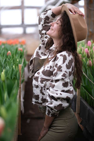 Young beautiful woman in hat posing looks at flowers in a greenhouse Tulipsの写真素材