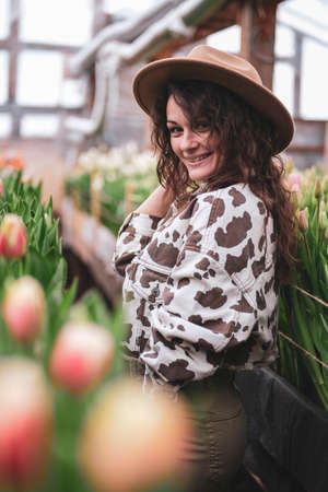 Young beautiful woman in hat posing looks at flowers in a greenhouse Tulipsの写真素材