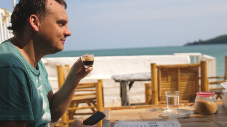 Attractive young man Drinking espressoa On Vocation Resort. Man Sitting On Cafe At Sea Beach. Guy...