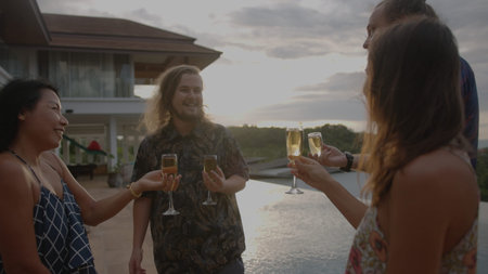 Group of friends having fun at poolside party clinking glasses with white wine by swimming pool on...
