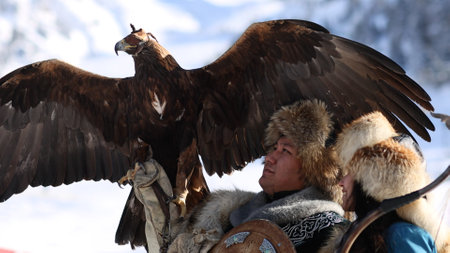 Almaty, Kazahstan - 2022. Kazakh Eagle Hunter traditional clothing, while hunting to the hare holding a golden eagle on his arm in mountain of Kazahstan and his wifeのeditorial素材
