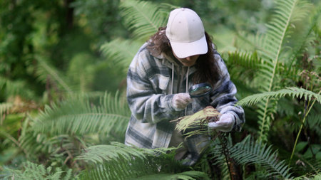 Female biologist is using a magnifying glass to look at plants with pest leaves. to collect data for analysis. Organic farming concept. Close upの写真素材